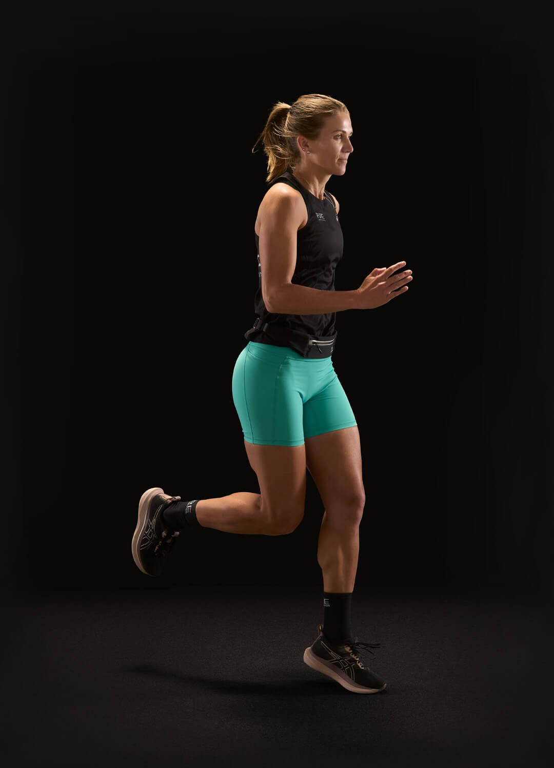 Woman running in athletic wear against a black background